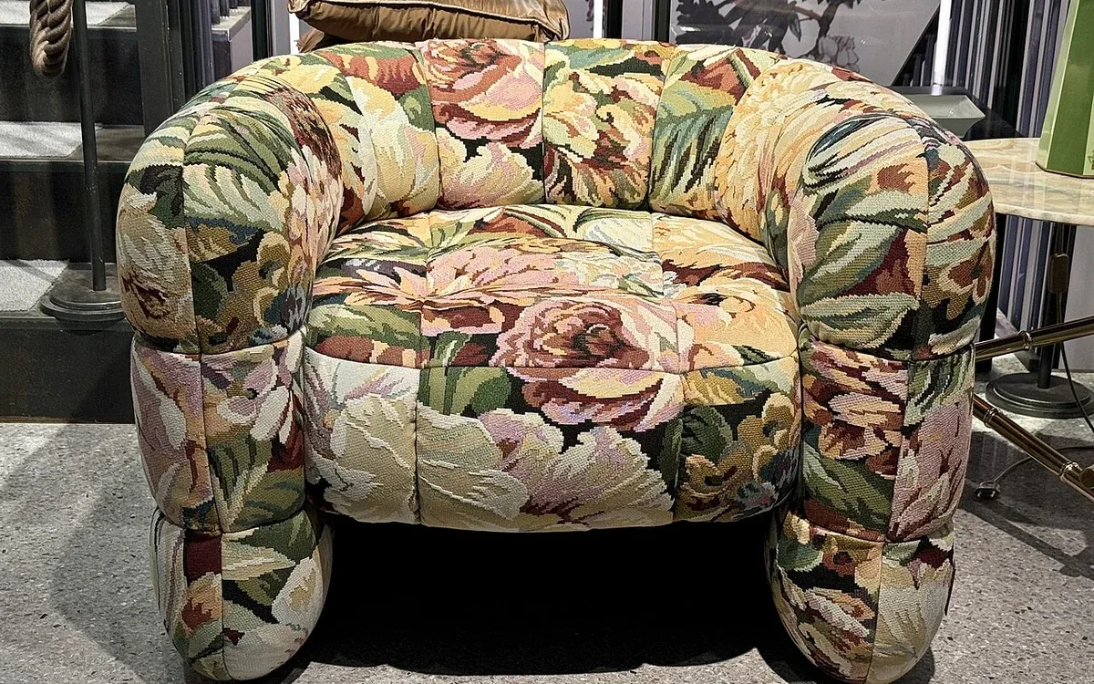 A wide upholstered armchair covered in a floral pattern stands on a carpeted floor