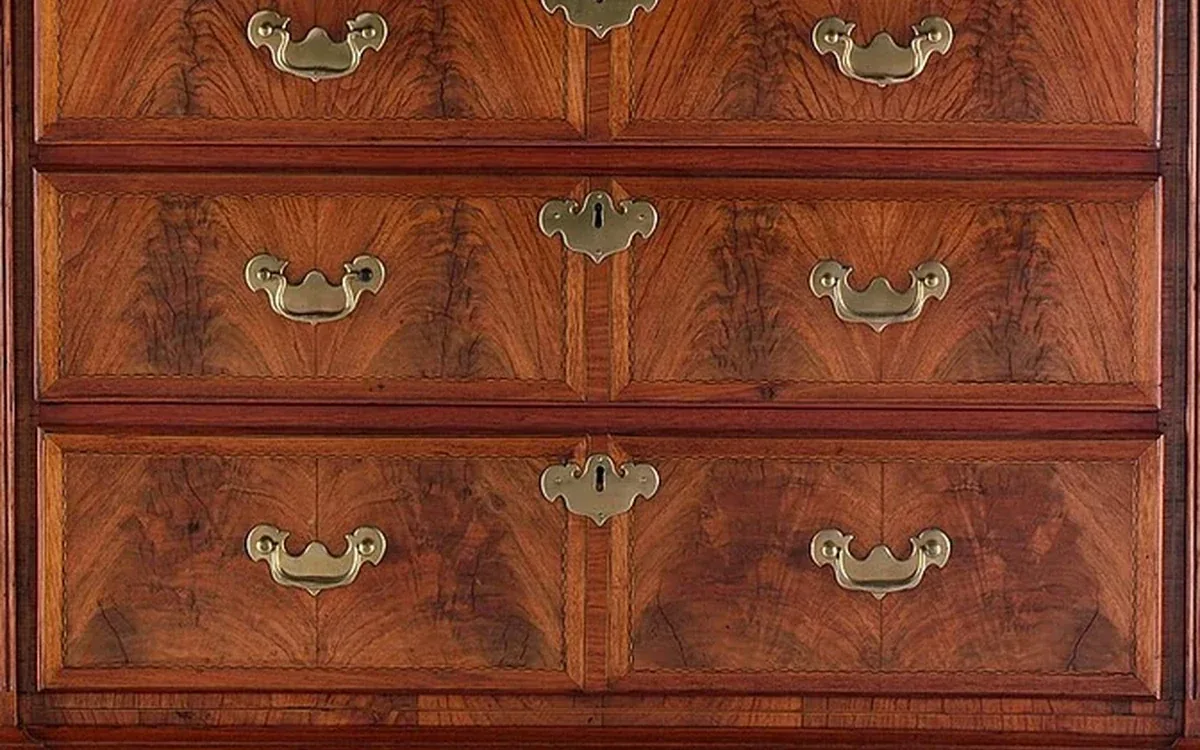 A close view shows wood grain, drawer fronts, curved brass handles and keyhole fittings on a wooden chest
