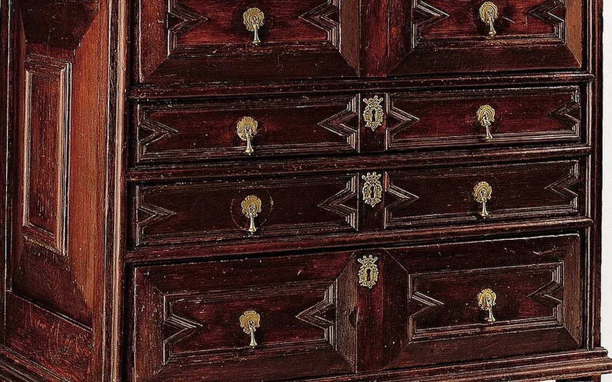 A close view shows dark wooden drawer fronts, decorative grain and brass handles on an antique chest