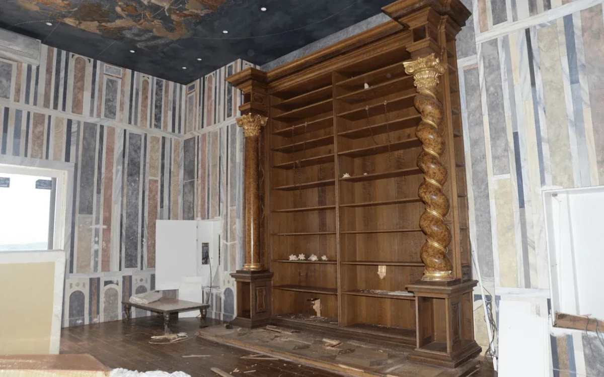A built-in wooden shelving unit stands beside partly exposed walls and a wooden floor during interior renovation
