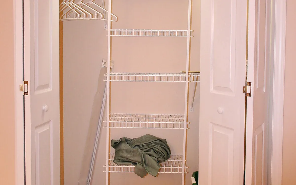 Two open white doors reveal a small walk-in closet with mostly empty wire shelves and a few folded belongings
