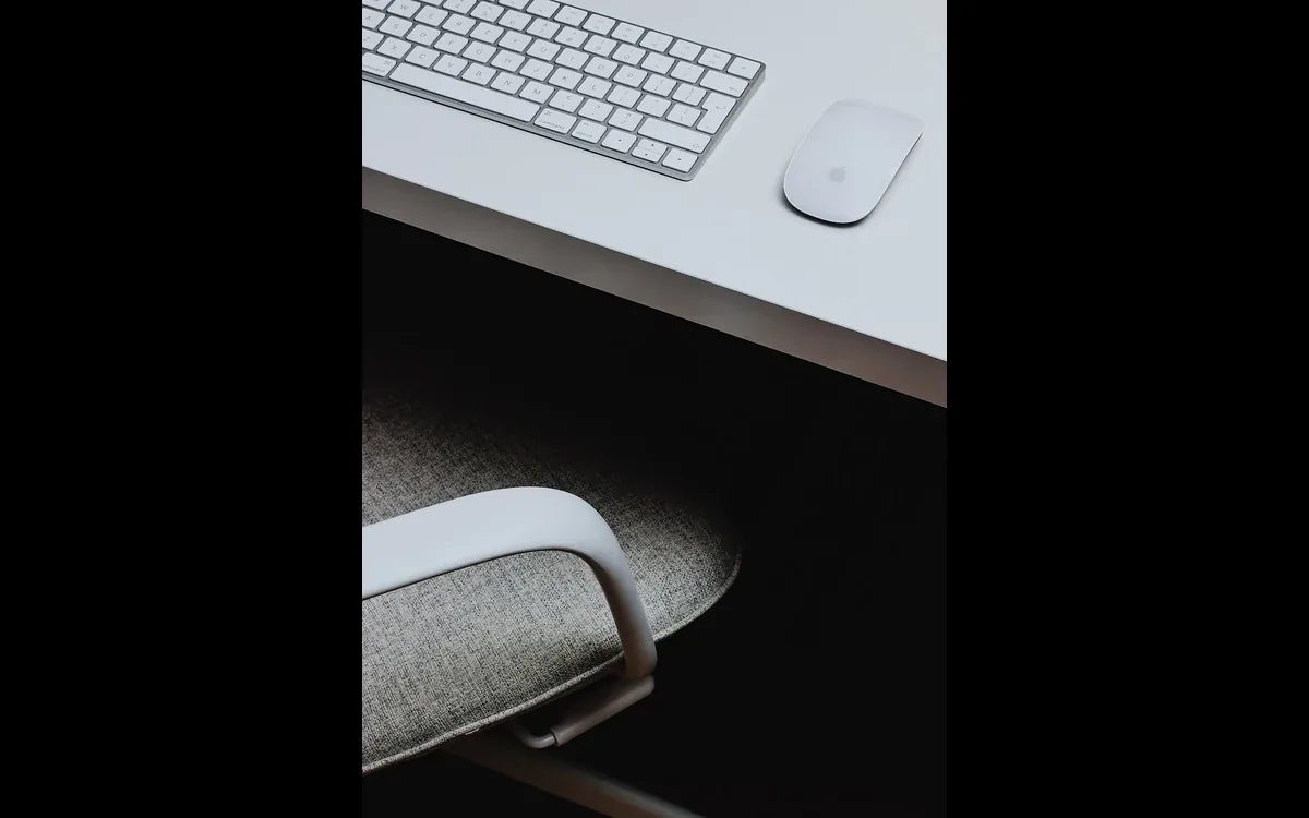 A keyboard and mouse rest on a pale desk above the arm of an upholstered chair