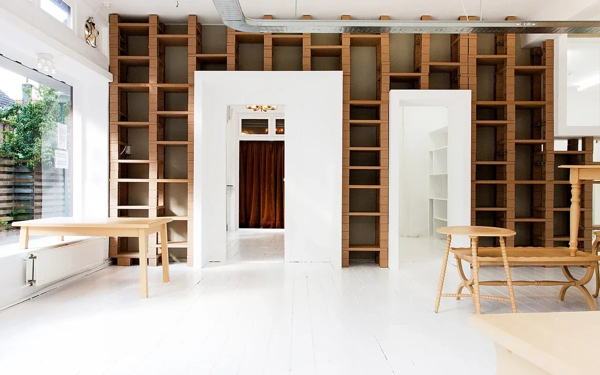 Tall empty wooden shelves surround a white doorway in a bright interior
