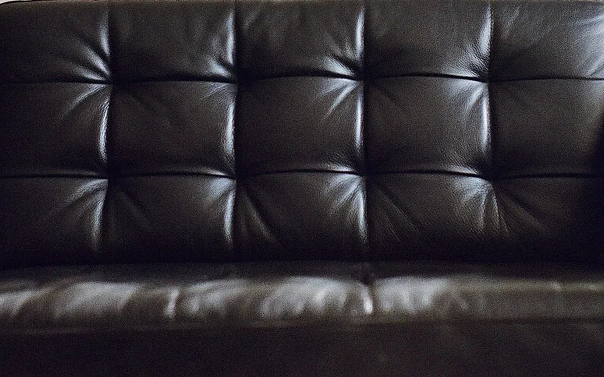 A dark leather sofa with broad padded cushions fills the foreground of a living area