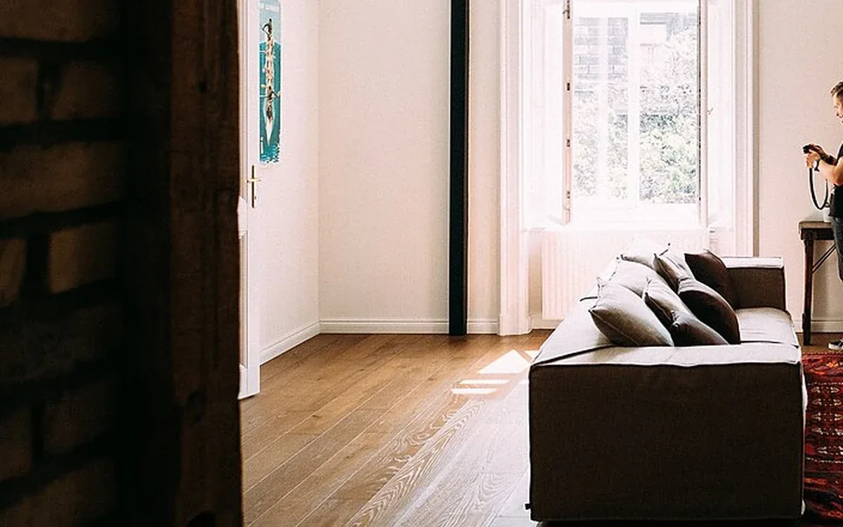 A dark sofa stands near a tall window beside a clear wooden floor