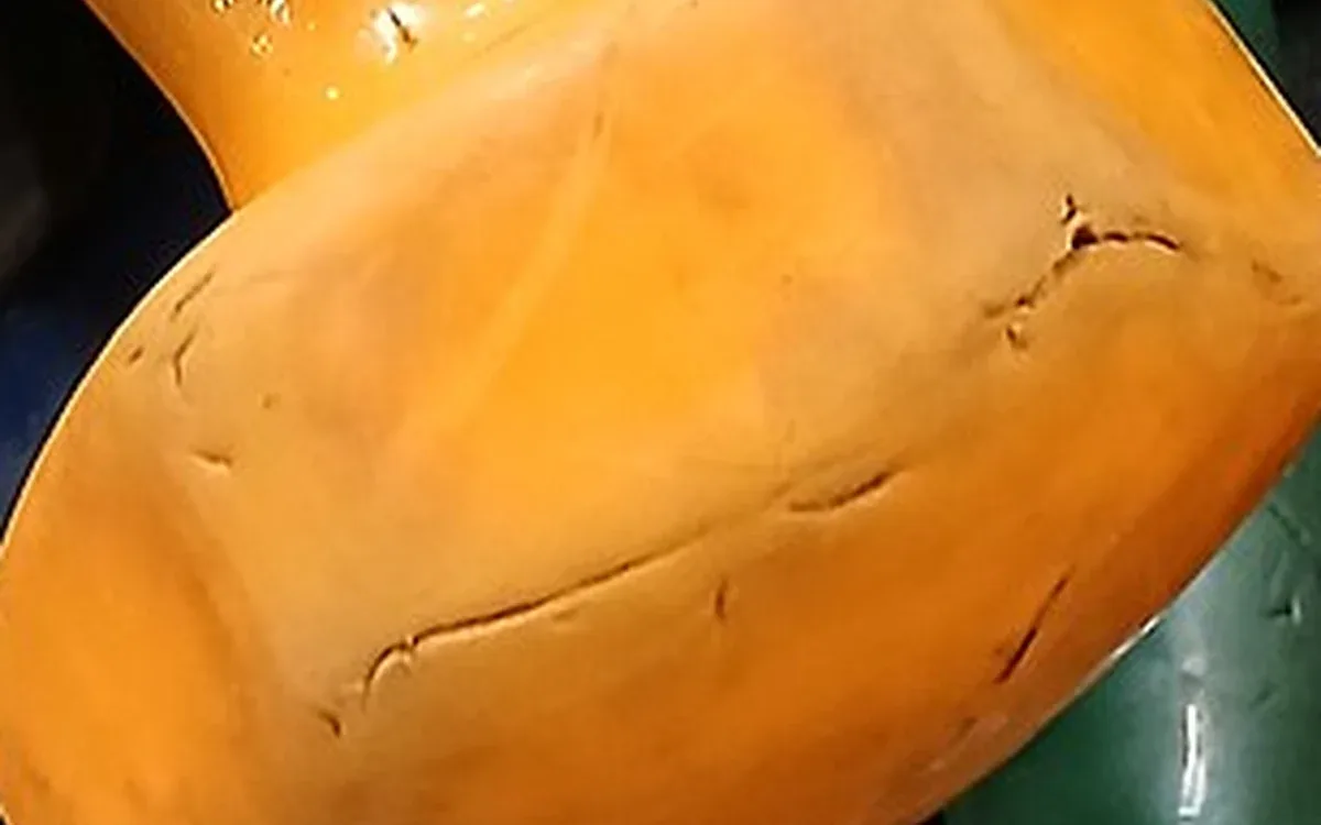 Close view of the rounded orange end of a coated dumbbell, with surface wear and other weights partly visible around it