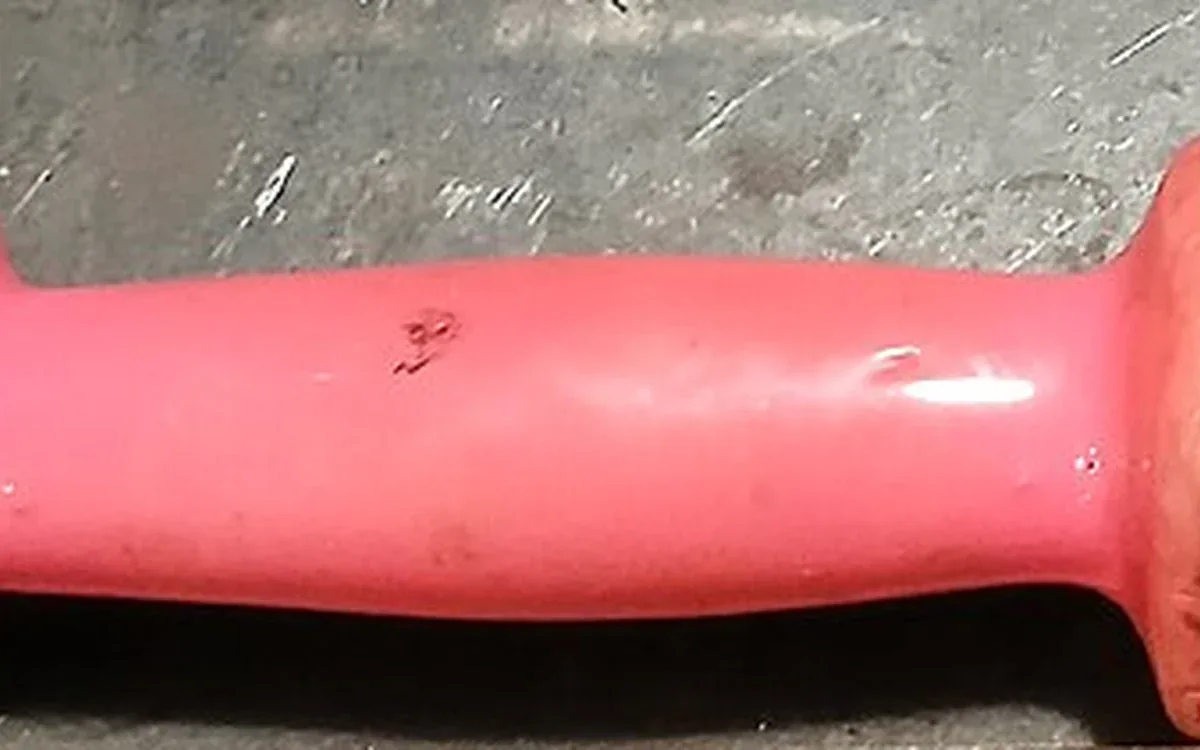 Close view of a red coated dumbbell handle resting on a dark shelf, with signs of everyday surface wear