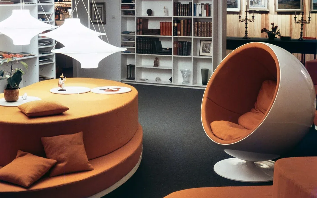 A round upholstered chair and low table sit near broad open shelves in a furnished interior
