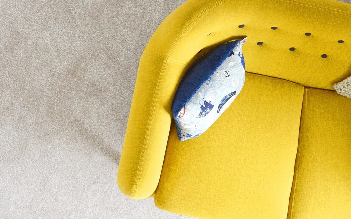 A yellow upholstered chair with a patterned cushion is viewed from above