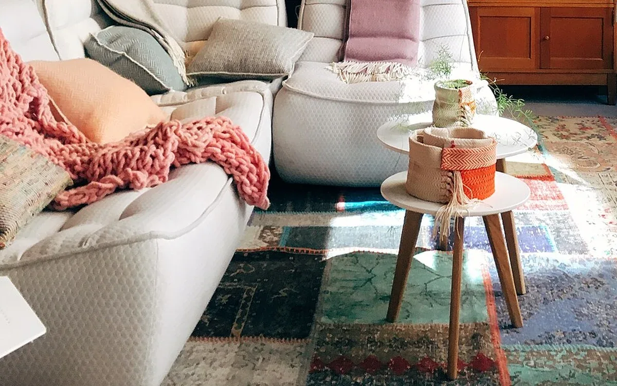 Pale upholstered seating and a low table stand on a patterned rug in a furnished interior