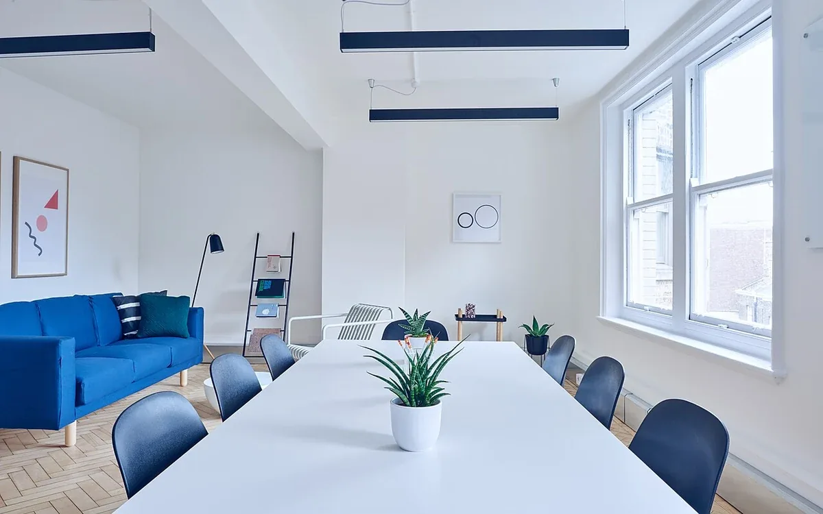 A long pale table and chairs occupy a bright room with a blue sofa and broad windows