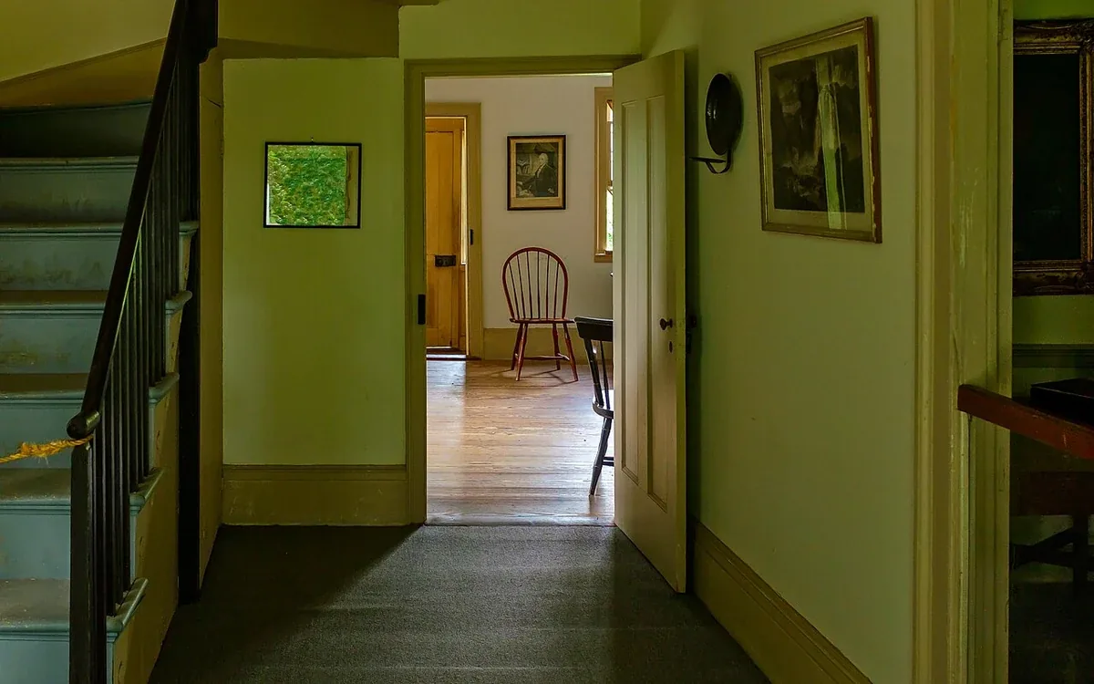 A pale green hallway leads through an open doorway to a room containing wooden chairs and framed artwork