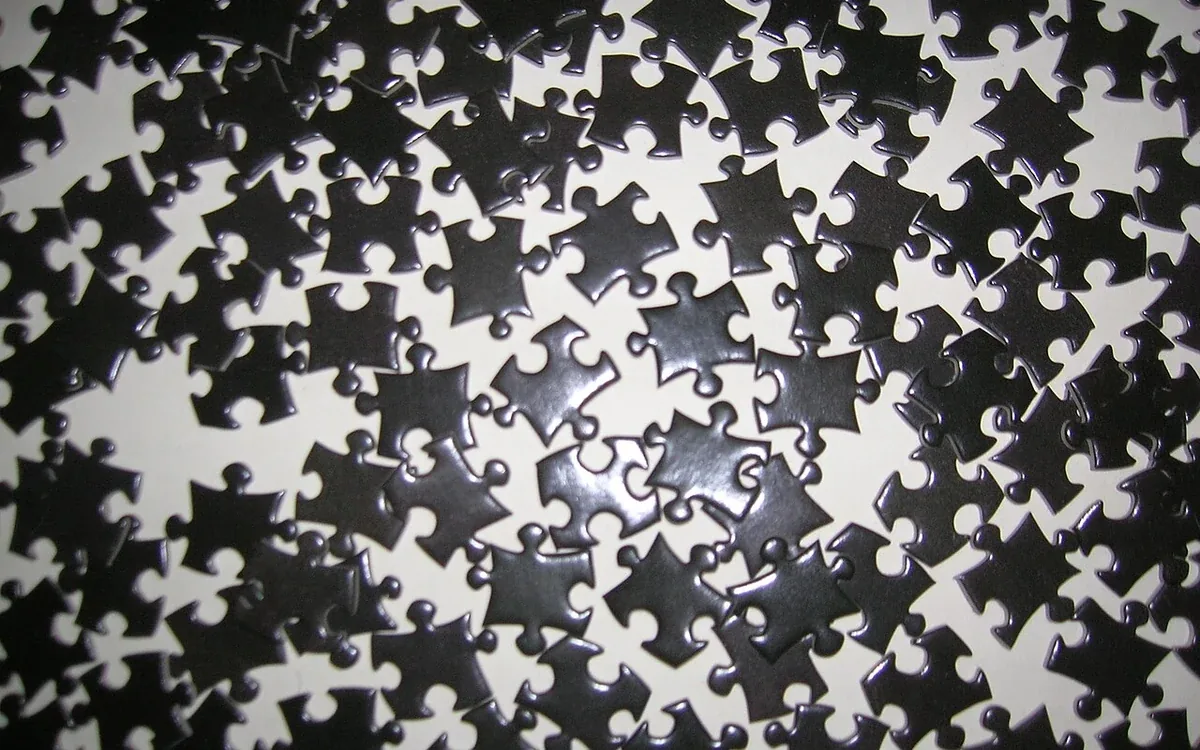 Scattered jigsaw puzzle pieces show plain light and dark backs, with their interlocking edges clearly visible