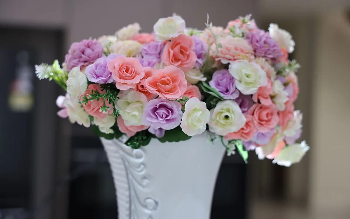 A pale decorative vase holds a bouquet of pink, purple and white flowers
