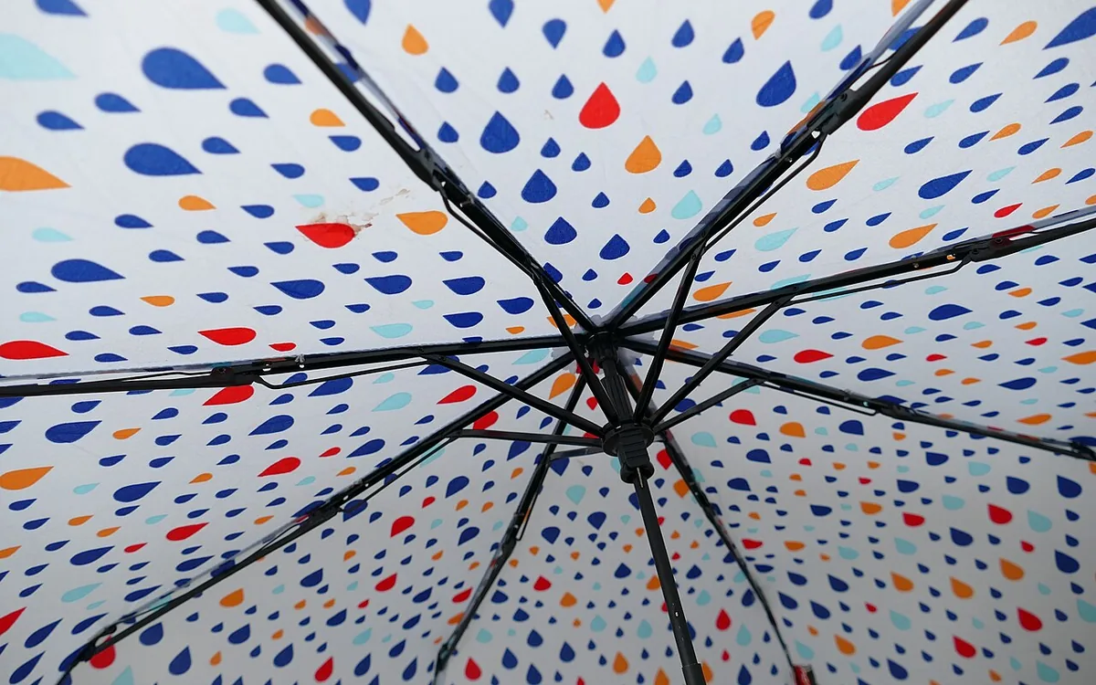 The underside of an open umbrella shows black ribs and a white canopy patterned with multicolored raindrops.