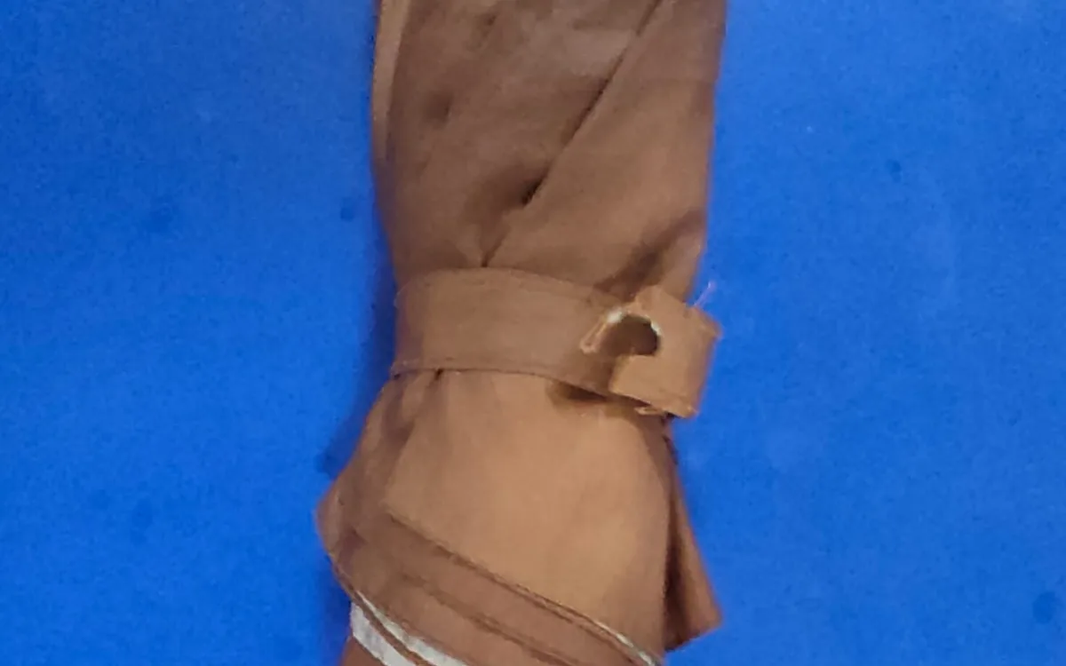 Close-up of a closed brown umbrella with a worn fastening strap and a frayed hole against a blue background.