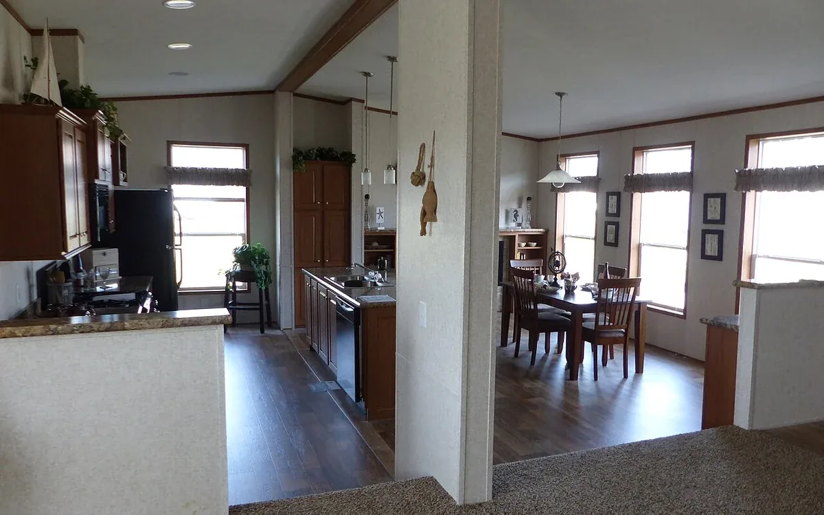 An open-plan kitchen and dining room has broad windows, light walls, a counter and wooden dining furniture