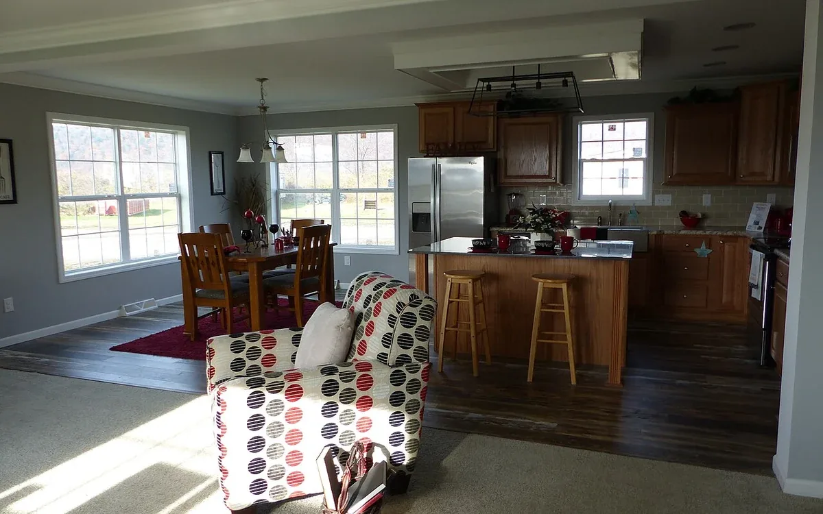A broad living and dining space contains a table, chair and patterned armchair, with a kitchen visible beyond