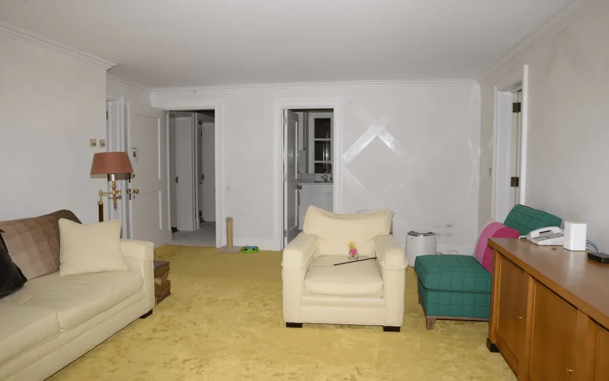 A pale sofa and armchair sit beside a wooden sideboard in a white-walled living room with an open doorway