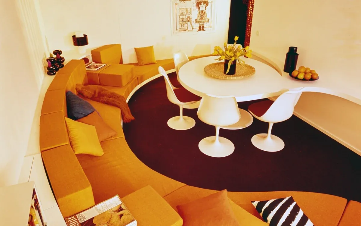 Orange upholstered seating curves around a small white table in a furnished room
