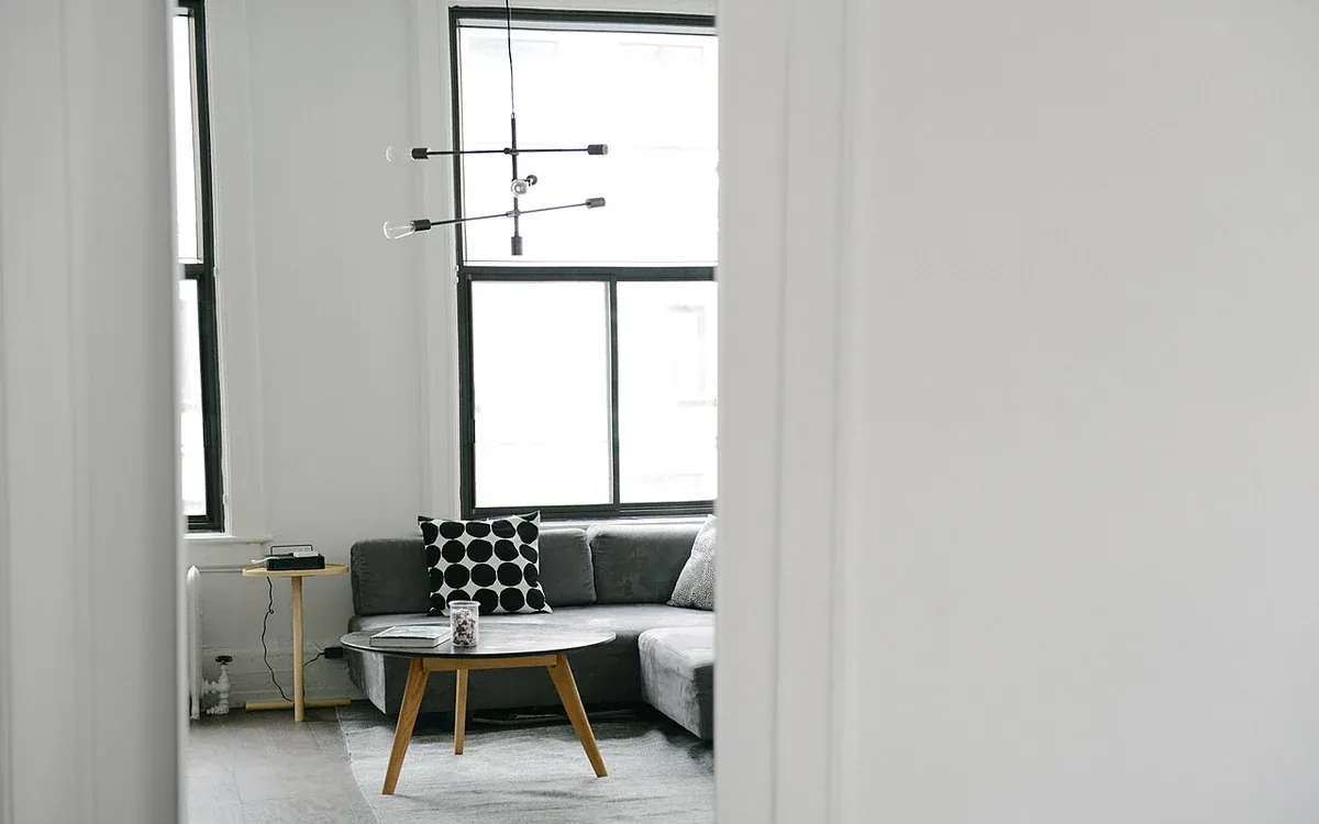 A pale doorway frames a sitting area with a sofa, patterned cushion and low table