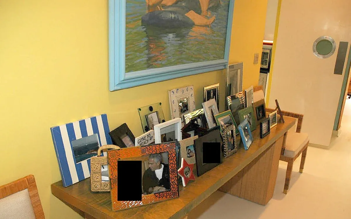 Many framed photographs rest on a wooden surface along a yellow wall