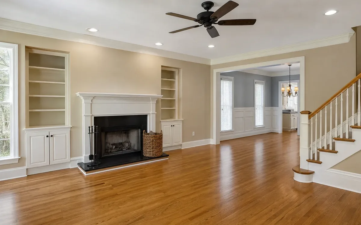Nearly empty living room with hardwood floors, open built-in shelves, a fireplace, a woven basket, and stairs on the right.