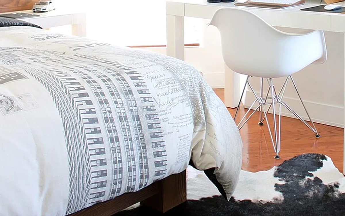 The lower edge of a bed and a pale desk chair share a wooden floor