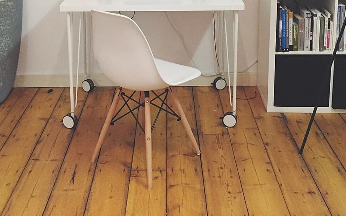 A pale desk chair stands on a wooden floor beside an open bookcase