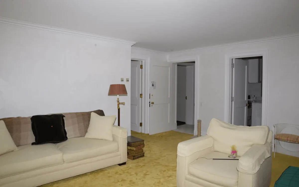 A light-colored sofa and matching armchair stand on a yellow carpet in a living room with several open doorways