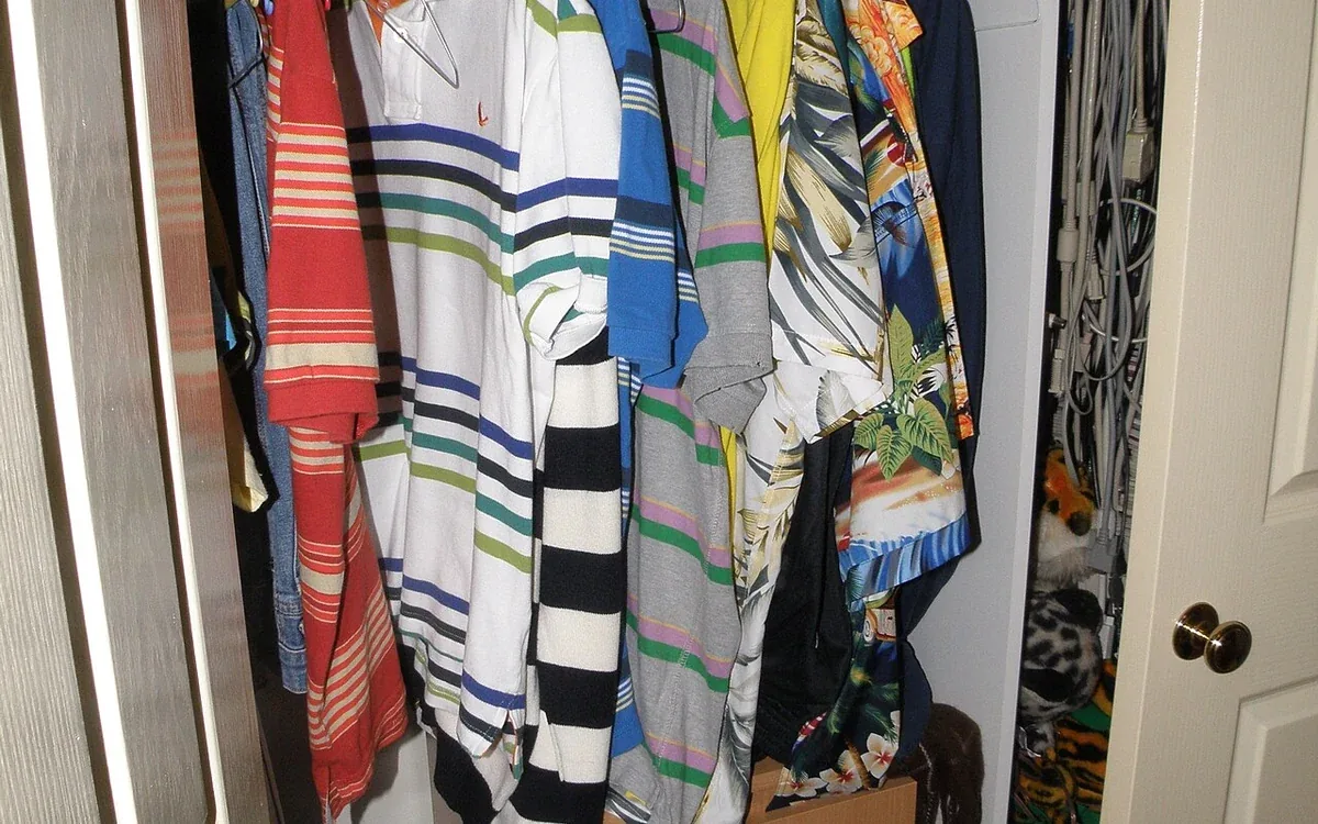 Shirts and other clothes hang above several cardboard-colored drawers inside a narrow open closet