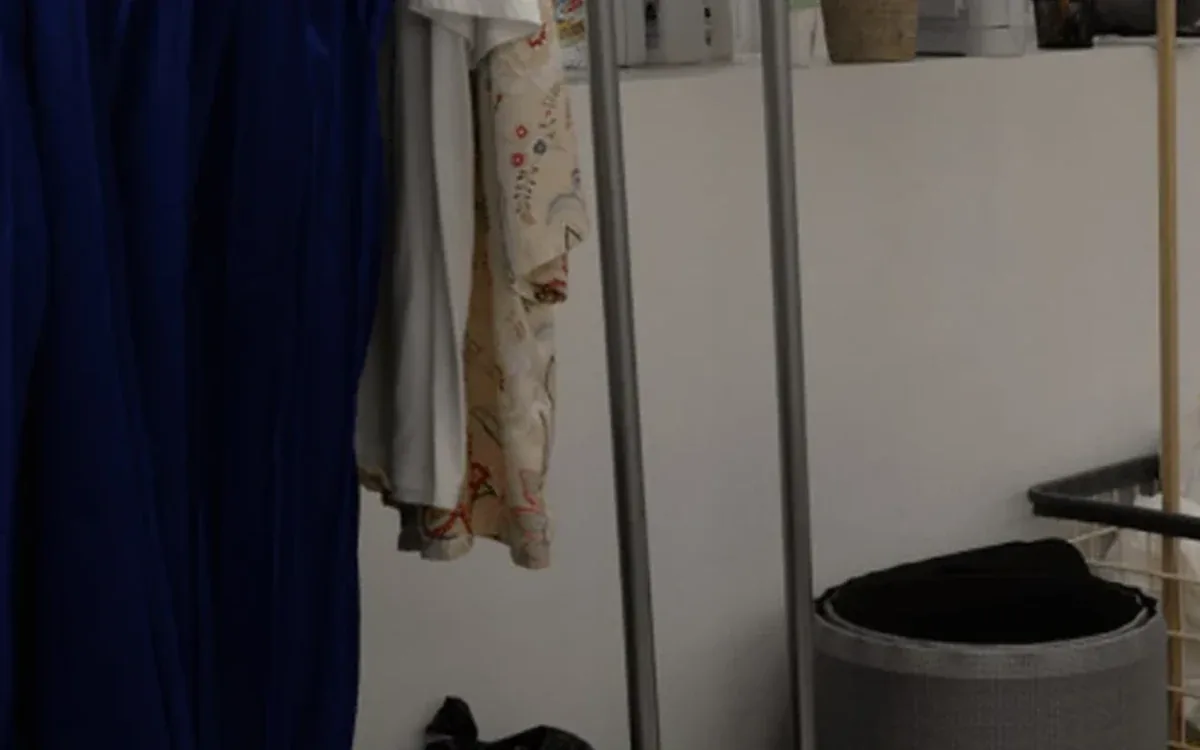 Dark clothes hang above black household containers on a pale tiled floor
