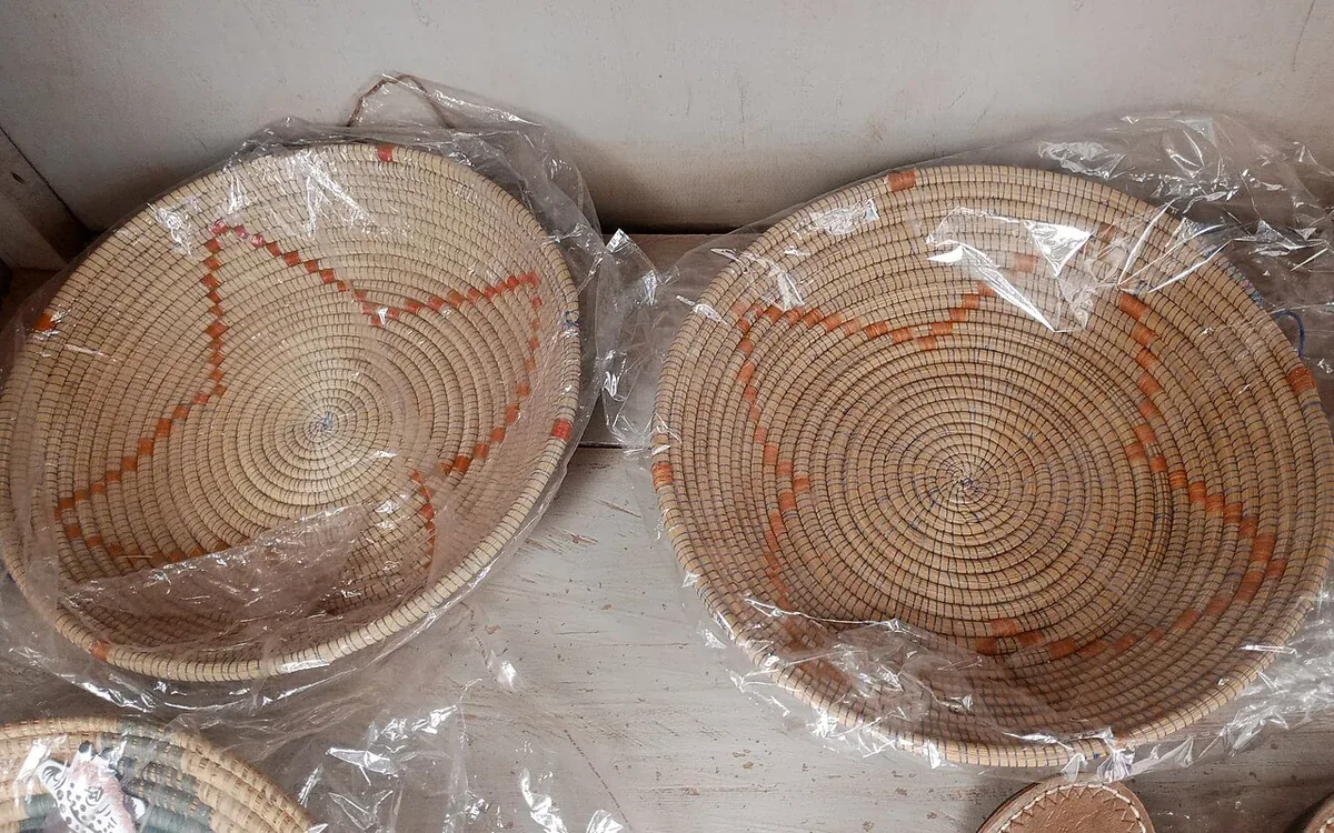 Several shallow round woven baskets with red and natural-colored patterns are covered with clear wrapping