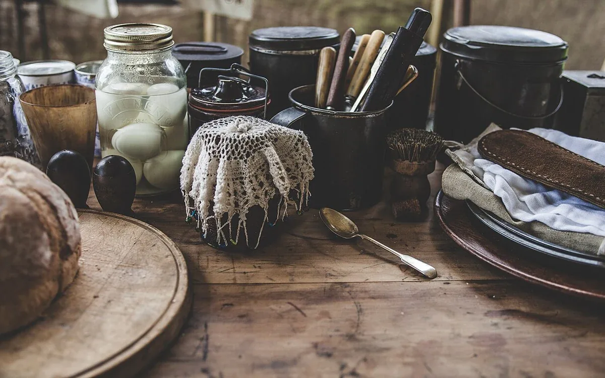 Cups, bowls, jars, utensils and a folded cloth are grouped together on a wooden kitchen surface
