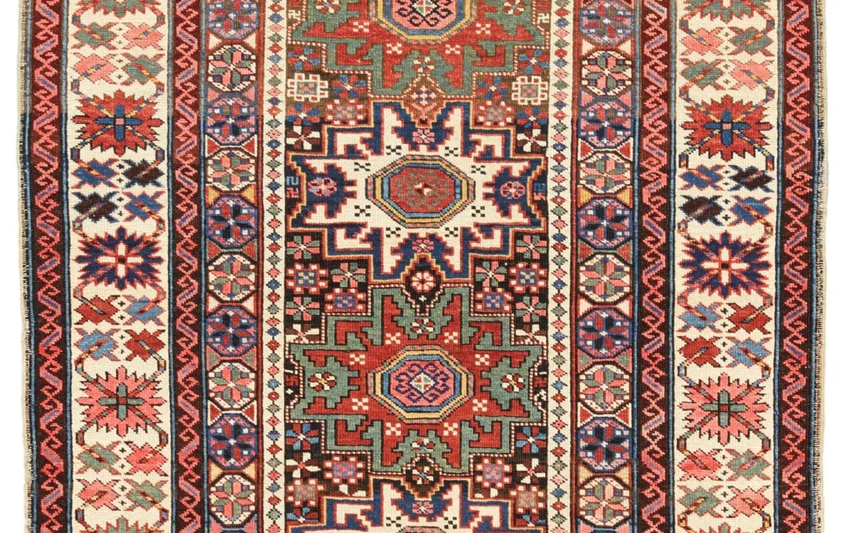 A patterned rug with a red central field, small geometric details and a cream border lies flat
