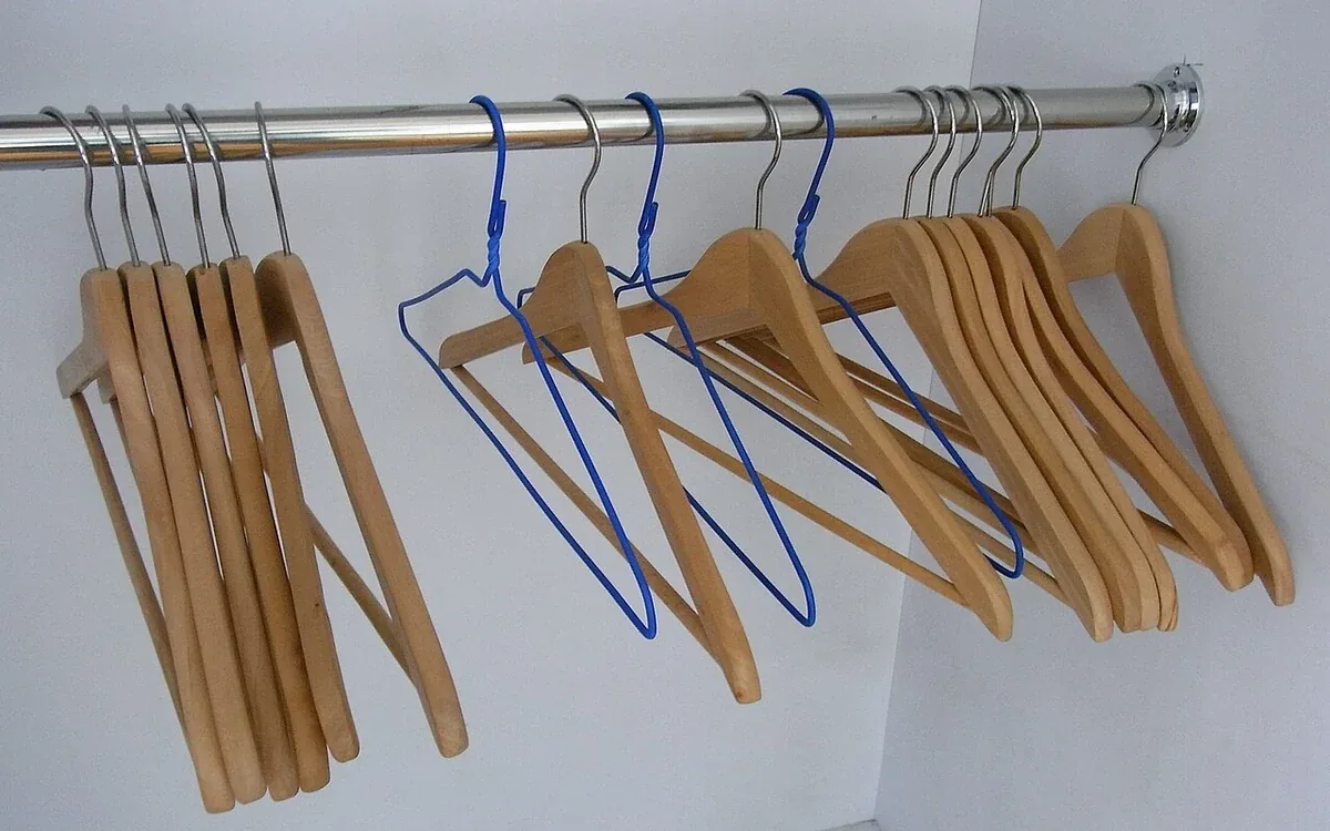 Empty wooden and metal clothes hangers hang from a horizontal closet rail against a pale wall