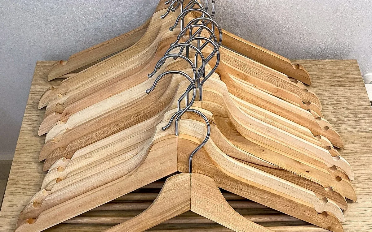 A grouped stack of empty wooden coat hangers rests against a pale surface, with metal hooks aligned at one end