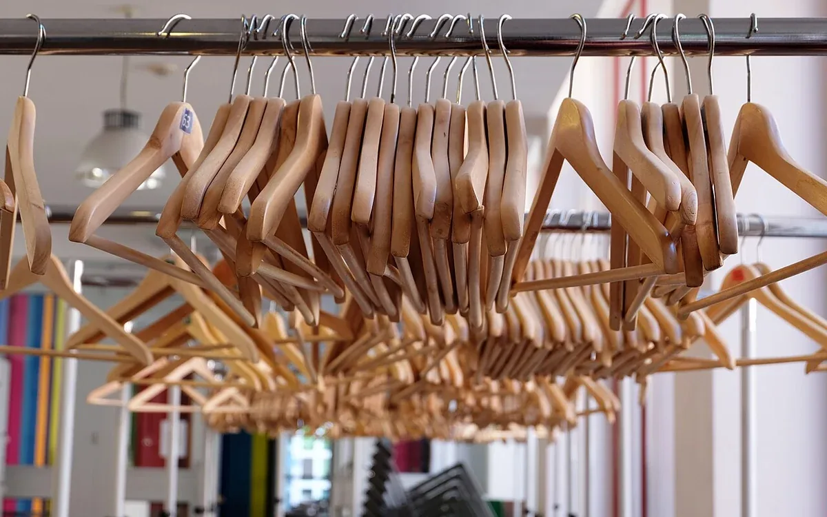 Many empty wooden clothes hangers with metal hooks hang close together from a horizontal rail