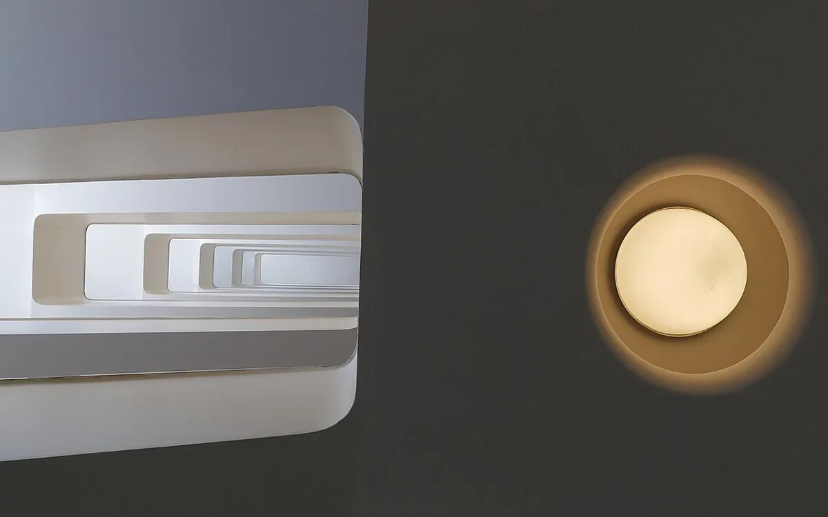 A circular ceiling light glows beside the curved white edges of an indoor staircase, viewed from below