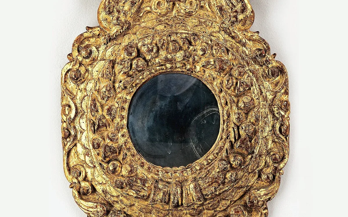 A small round mirror sits within an ornate gold-colored frame with scrolling decorative edges