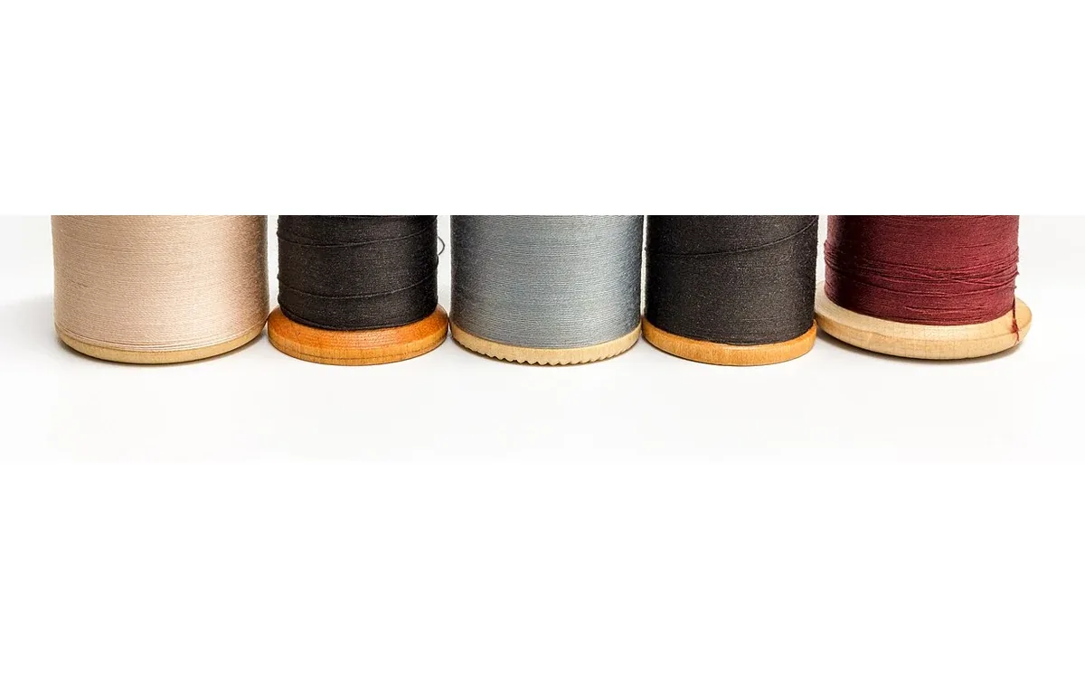 Five wooden thread spools wrapped with cream, dark brown, gray, black and burgundy thread sit in a row