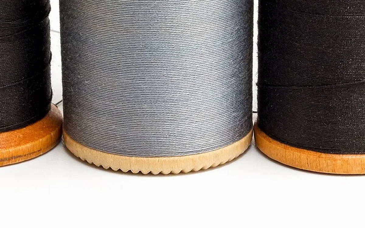 Three wooden thread spools wrapped with dark and gray thread stand together, with their wooden bases visible