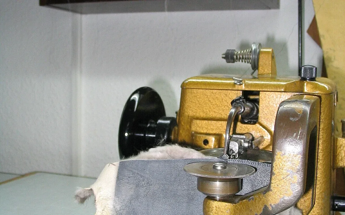A gold-colored sewing machine with exposed metal working parts and a black side wheel stands on a work surface