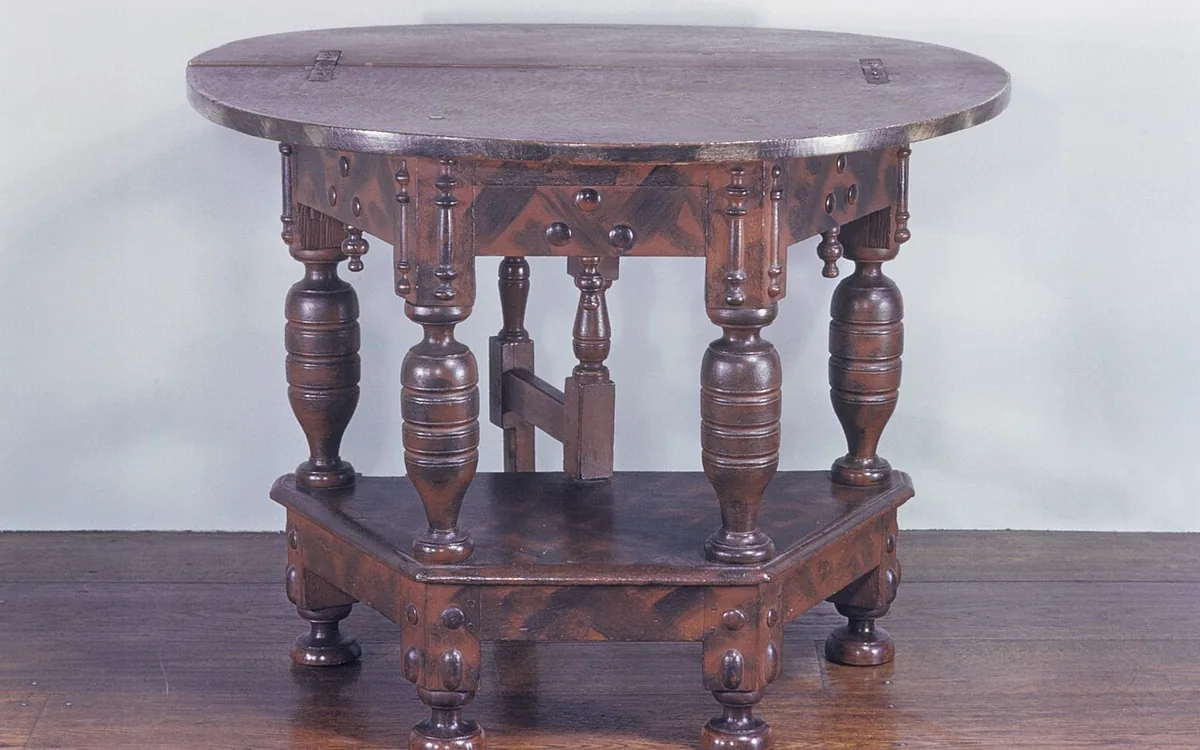 Dark wooden table with a rounded hinged tabletop, decorative turned legs and a lower shelf on a wooden floor.