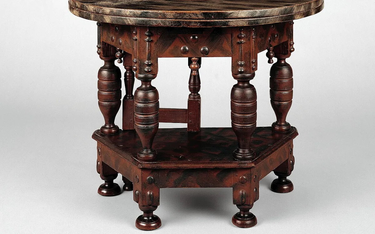 Close-up of an ornate dark wooden table with turned legs and a lower shelf against a light background.