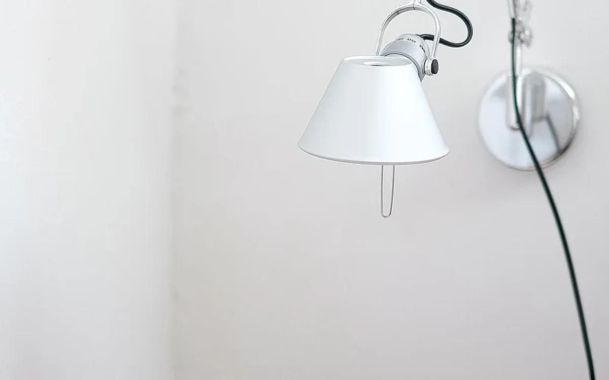 A white adjustable lamp with a metal bracket hangs against a pale wall