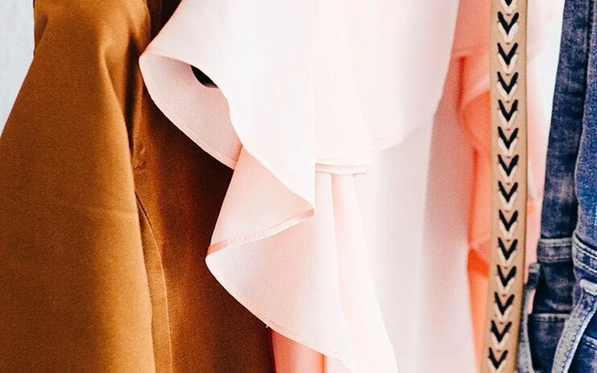 Close-up detail shows the fabric of a brown coat and pale pink shirt beside a patterned strap
