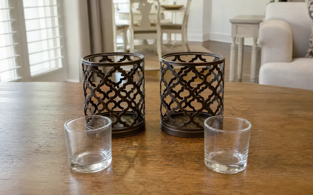 Two tall dark metal lattice candleholders stand behind two small clear glass candleholders on a wooden table.