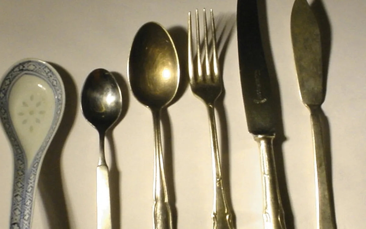 A ceramic spoon rest, two spoons, a fork, a knife, and a spreader arranged on a light surface