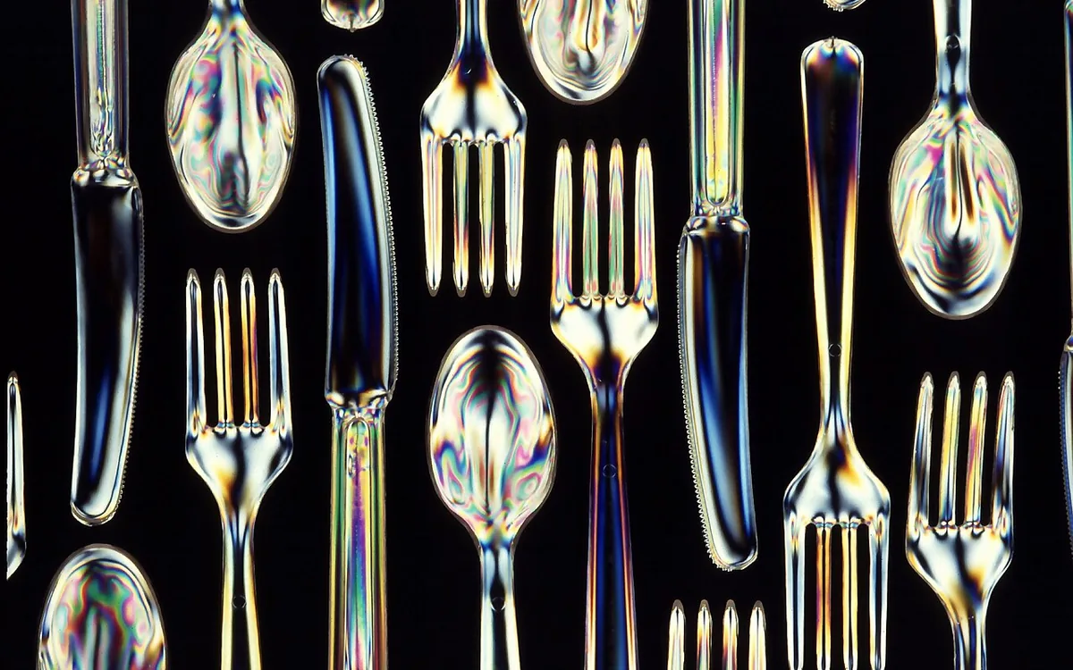 Reflective spoons, forks, and knives arranged against a black background